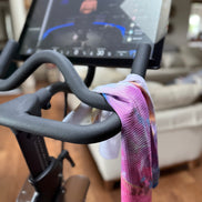 Close-up of a stationary bike with the colorful Bloom quick dry towel draped over it. Bloom design is based on Isaiah 35:2.