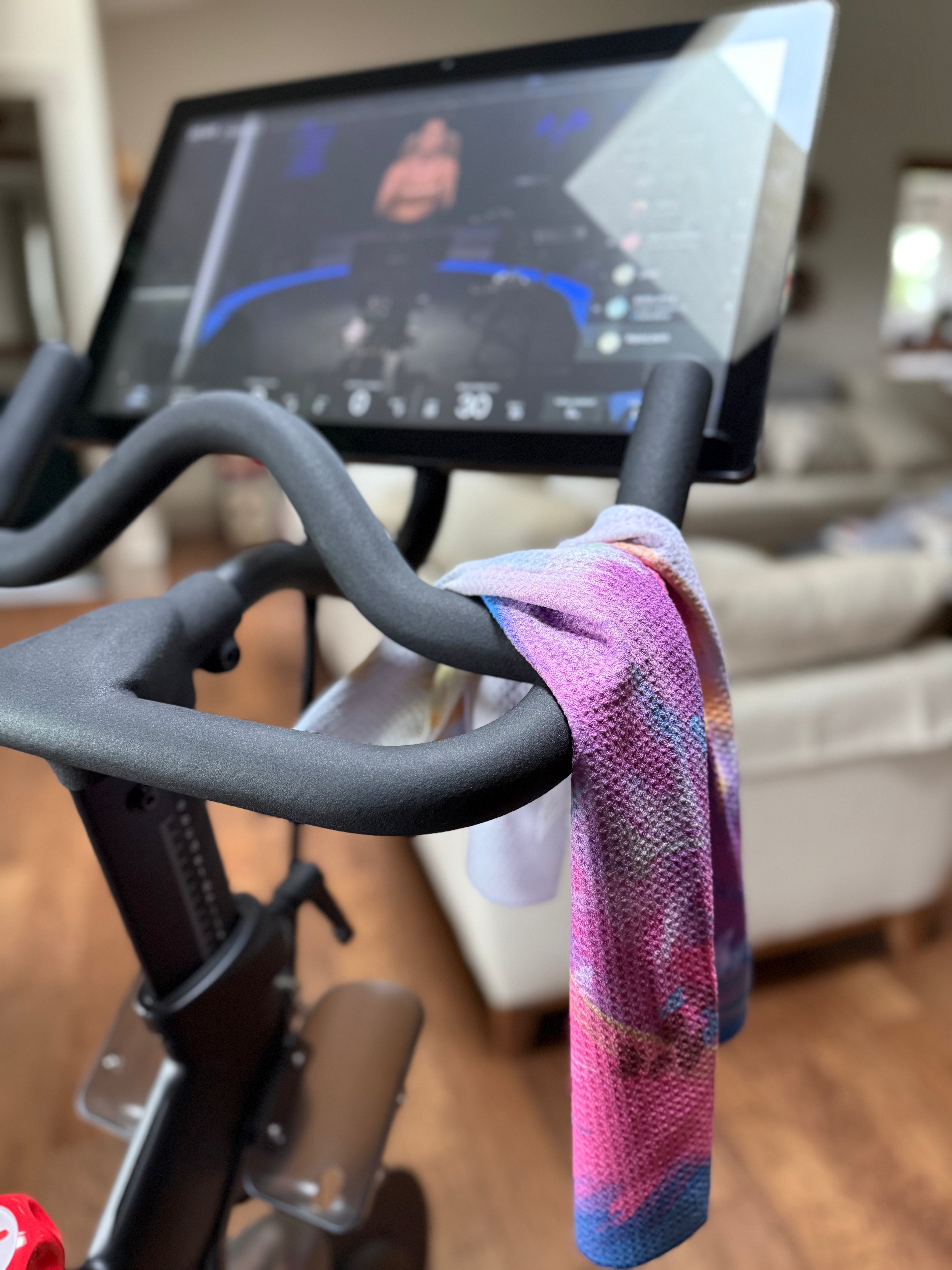 Close-up of a stationary bike with the colorful Bloom quick dry towel draped over it. Bloom design is based on Isaiah 35:2.