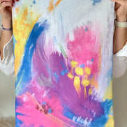 Person holding the Bloom quick-dry towel, a colorful abstract floral painting based on Isaiah 35:2.