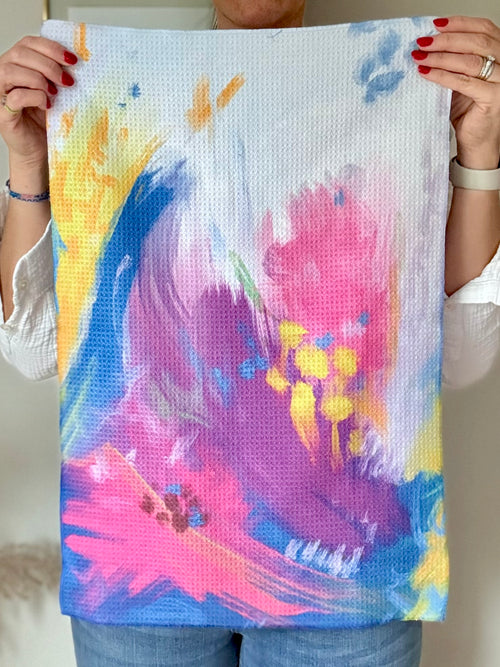 Person holding the Bloom quick-dry towel, a colorful abstract floral painting based on Isaiah 35:2.