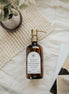 Amber glass Love Is... multipurpose Gratitude Bottle with gold pump on towels.