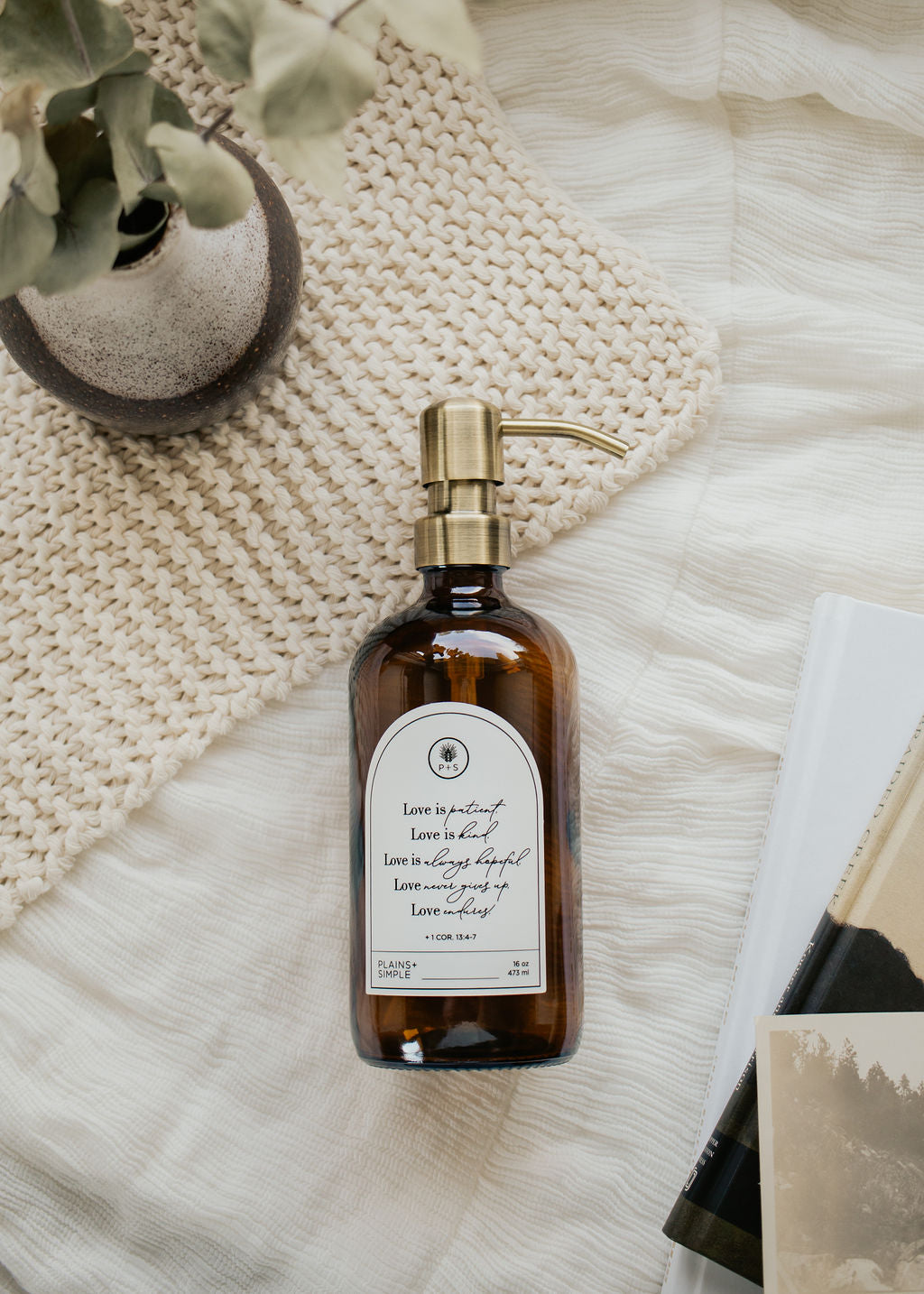 Amber glass Love Is... multipurpose Gratitude Bottle with gold pump on towels.