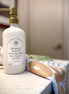 A gold pump on a white 16 oz glass reusable soap or lotion bottle with a printed label reading 'Love is patient, Love is kind, Love is always hopeful. Love never gives up, Love endures! 1 Cor. 13:4-7' next to a beautifully printed hand towel based on the Matthew 17 mustard seed verse.