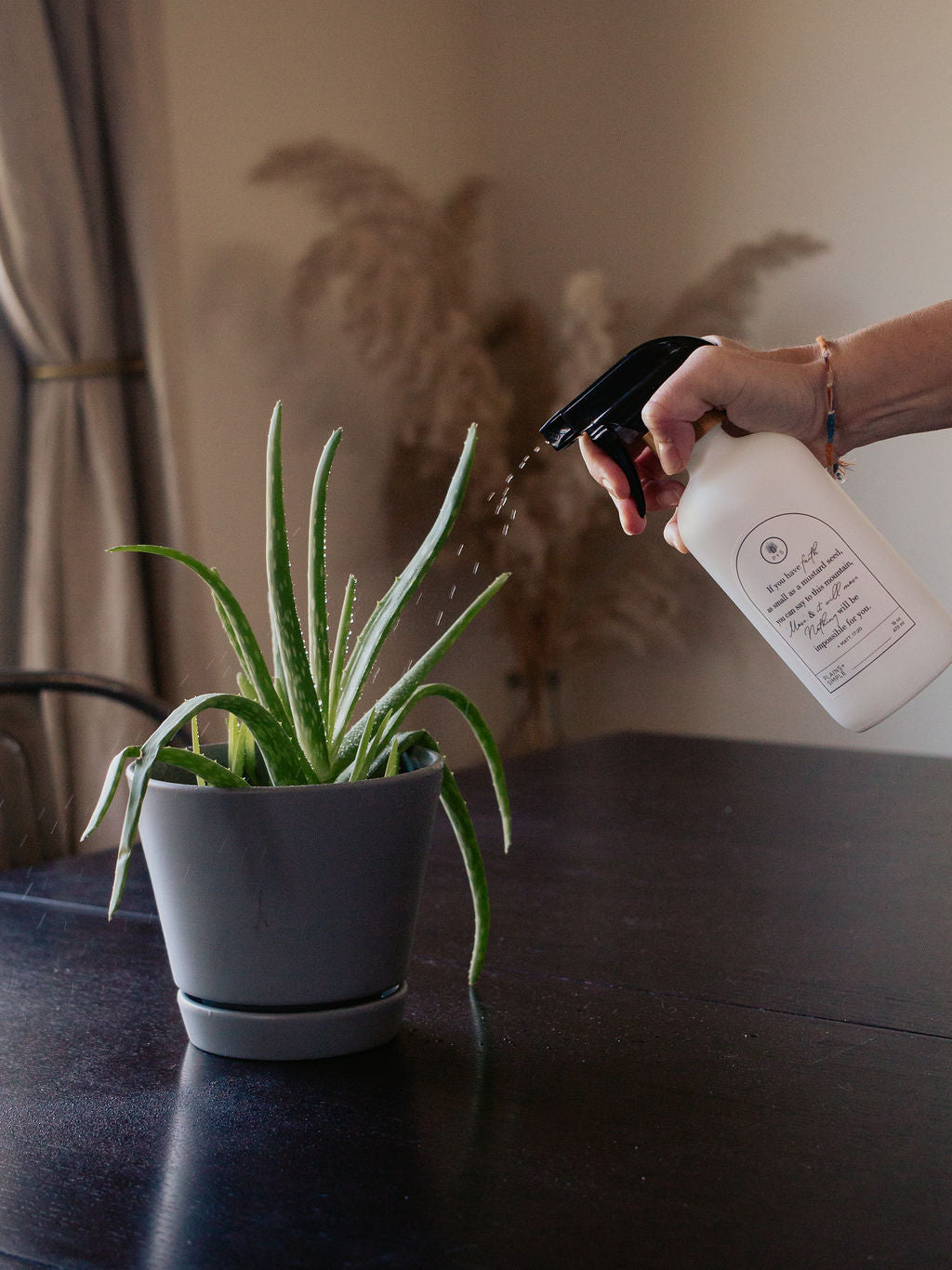 White glass Mustard Seed multipurpose Gratitude Bottle with spray pump watering a plant.