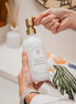 White glass I Can Do All Things multipurpose Gratitude Bottle with gold pump being used by the bathroom sink.