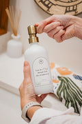 White glass I Can Do All Things multipurpose Gratitude Bottle with gold pump being used by the bathroom sink.
