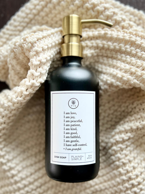 Black glass Fruits of the Spirit dish soap Gratitude Bottle with gold pump on a towel.