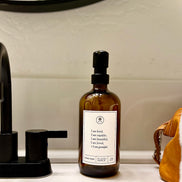 Amber glass I am Kind hand soap  Gratitude Bottle with black pump next to bathroom sink.