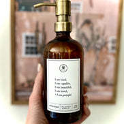 Hand holding an Amber glass I am Kind hand soap  Gratitude Bottle with gold pump.