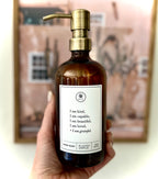 Hand holding an Amber glass I am Kind hand soap  Gratitude Bottle with gold pump.