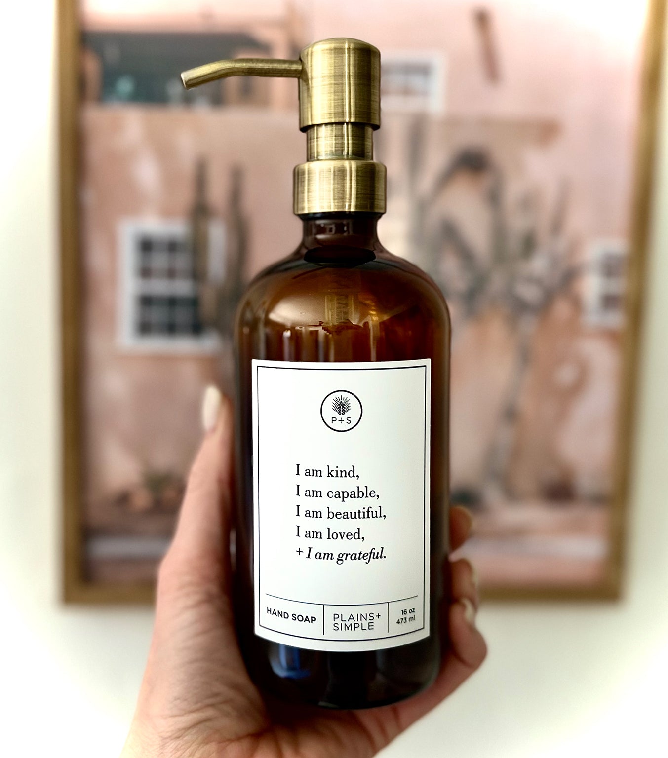 Hand holding an Amber glass I am Kind hand soap  Gratitude Bottle with gold pump.