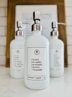 White glass I am Kind hand soap Gratitude Bottle with silver pump with matching dish soap and lotion bottles on the kitchen counter.