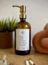 Amber glass I am Salt & Light lotion Gratitude Bottle with gold pump on a bathroom shelf with jewelry.