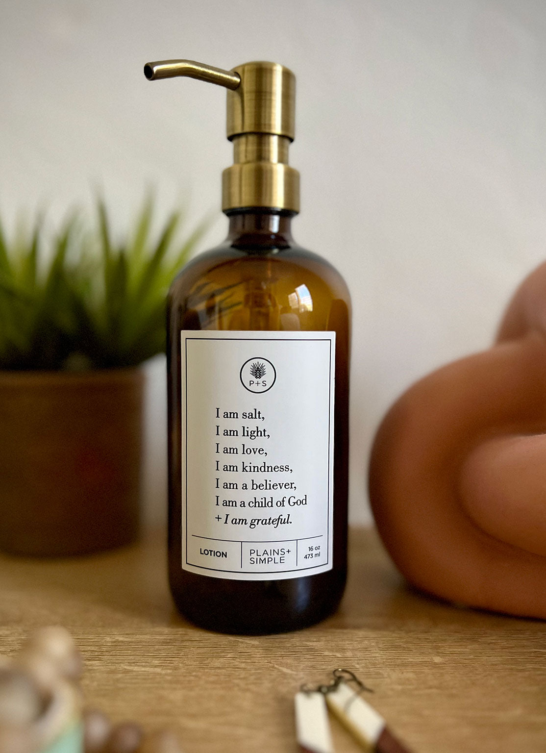 Amber glass I am Salt & Light lotion Gratitude Bottle with gold pump on a bathroom shelf with jewelry.