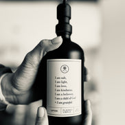 Black glass I am Salt & Light lotion Gratitude Bottle with black pump being held by hands.
