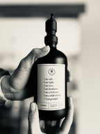 Black glass I am Salt & Light lotion Gratitude Bottle with black pump being held by hands.