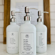 White glass I am Salt & Light lotion Gratitude Bottle with silver pump shown with matching hand soap and dish soap bottles on the kitchen counter.