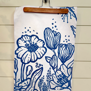 Floral patterned blue & white Presence quick-dry towel hanging on a wooden hanger against a wooden wall.