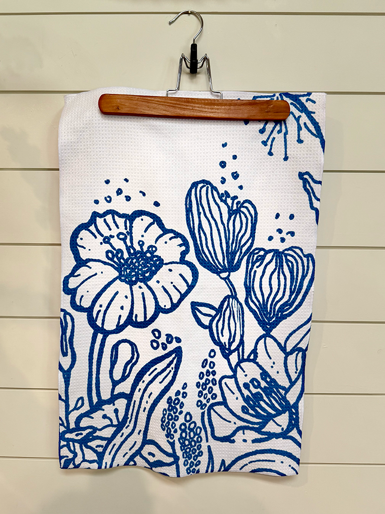 Floral patterned blue & white Presence quick-dry towel hanging on a wooden hanger against a wooden wall.