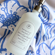 White glass Love Is Gratitude Bottle with silver pump on a blue and white floral patterned hand towel.