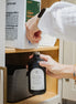 Refilling a black glass Seasons multipurpose Gratitude Bottle with hand soap.