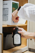 Refilling a black glass Seasons multipurpose Gratitude Bottle with hand soap.