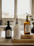 Three Trust multipurpose glass Gratitude Bottles with pump dispensers on a wooden surface in a kitchen setting.