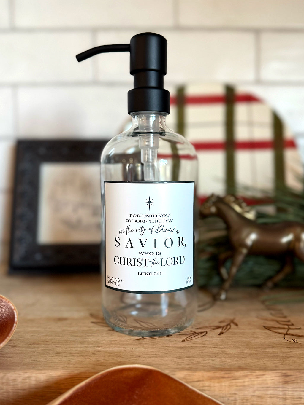 Reusable glass Christmas Gratitude Soap dispenser amongst Christmas decorations.