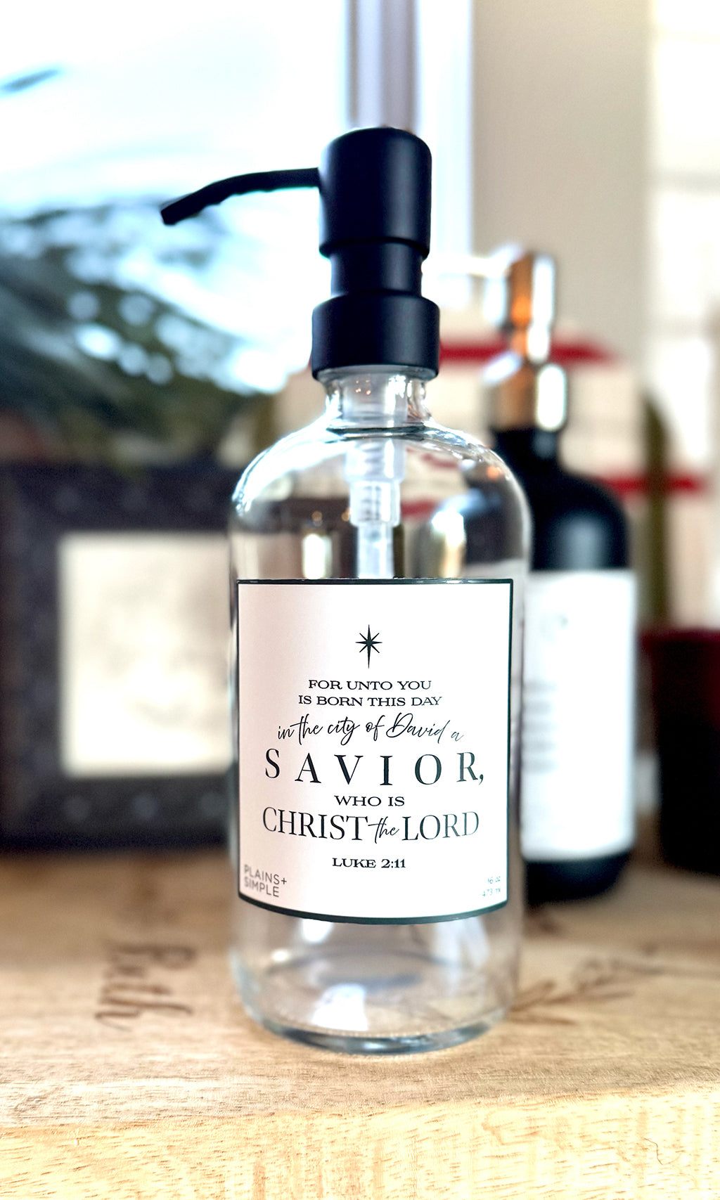 Reusable glass Christmas Gratitude Soap dispenser amongst Christmas decorations.