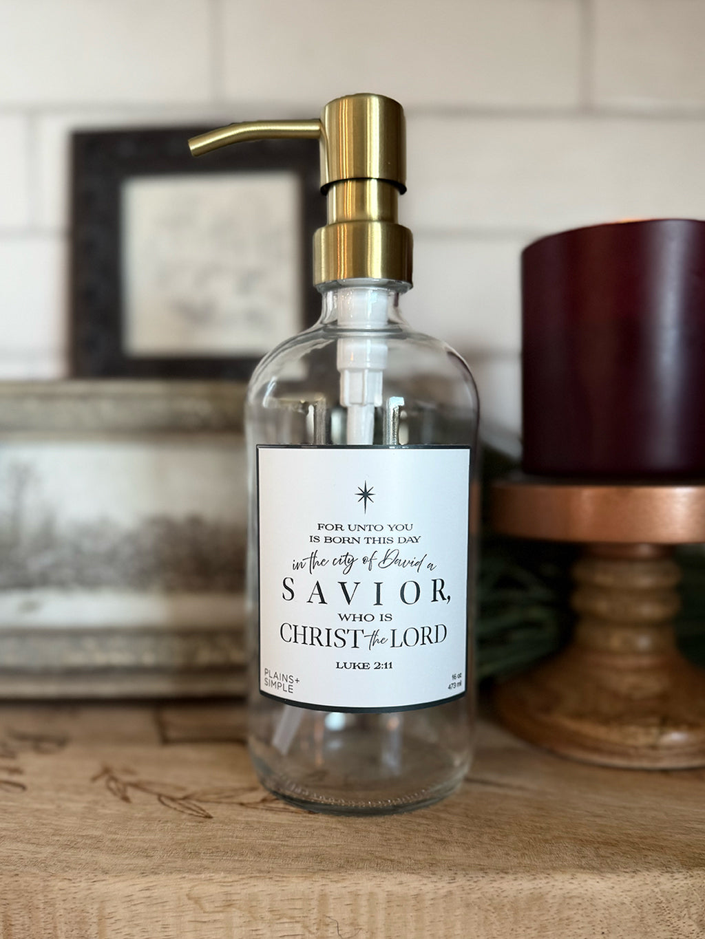 Reusable glass Christmas Gratitude Soap dispenser amongst Christmas decorations.