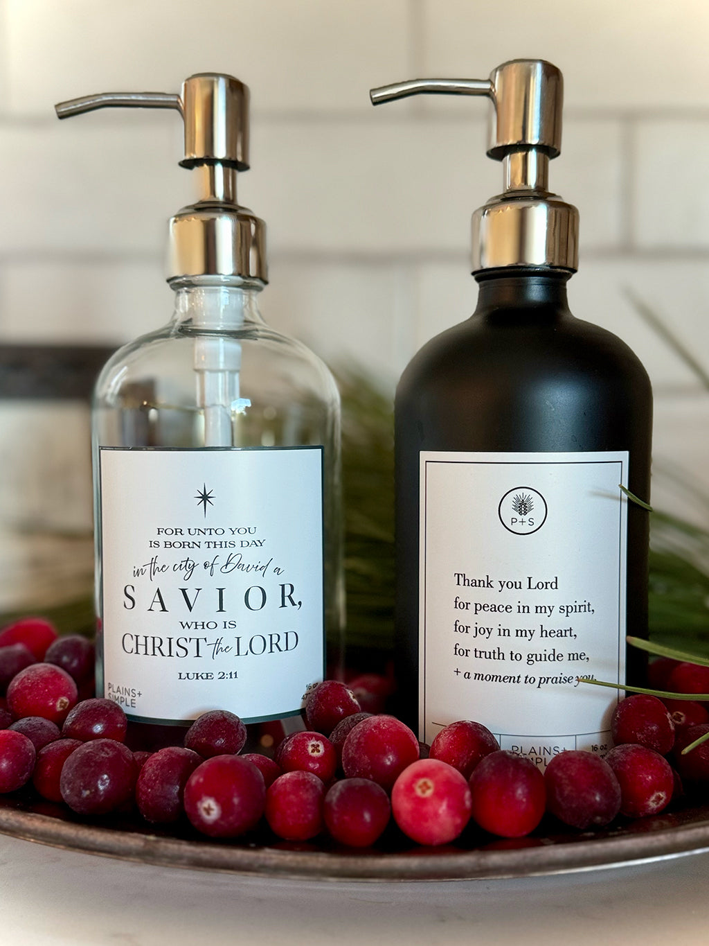 Reusable glass Christmas Gratitude Soap dispenser next to lotion gratitude bottle amongst Christmas decorations.